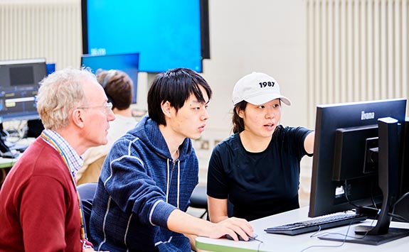 Two students and their lecturer discussing an item displayed on their computer